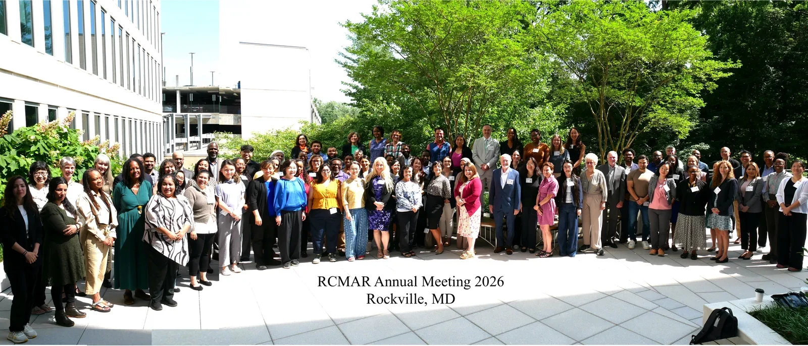 Group of approximately 100 people standing outside with trees and buildings in the background, labeled RCMAR Annual Meeting 2026, Rockville MD