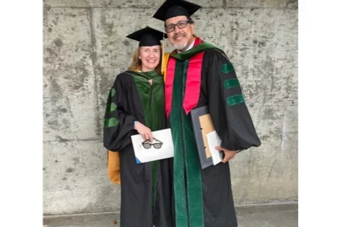 Gerardo Moreno and Carol Mangione holding awards while in cap and gown.