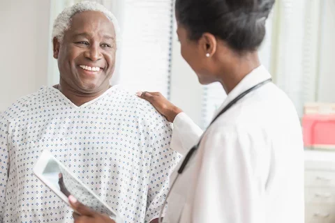 A man in a hospital gown smiles at a doctor in a white lab coat.