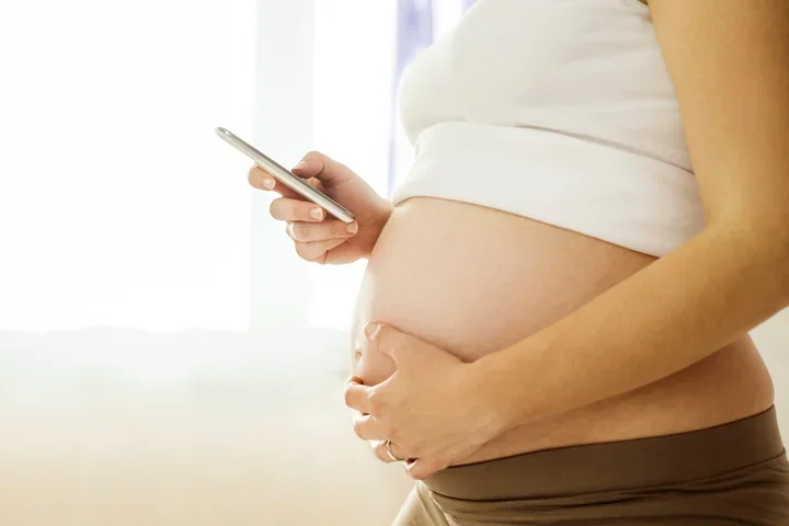 Side view of a pregnant woman holding a phone.