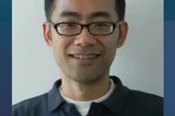 Man's face smiling with glasses and dark hair with blue collared shirt