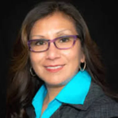 Lourdes Guerrero is wearing glasses, a teal collar shirt, and a black jacket.