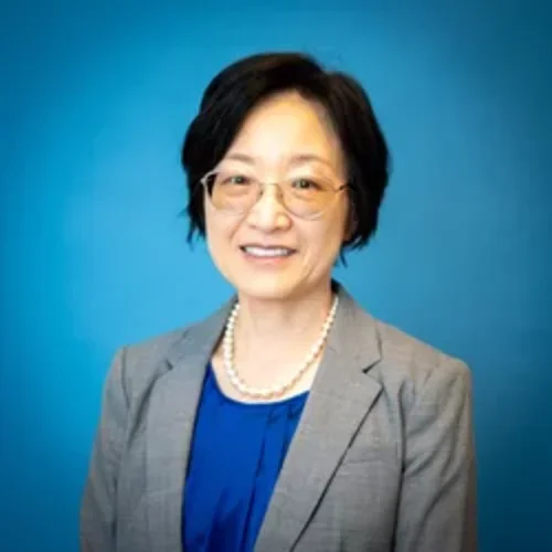Sarah Choi is pictured here with glasses, pearl necklace, blue shirt, and grey jacket.