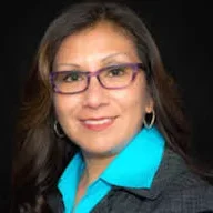 Lourdes Guerrero is wearing glasses, a teal collar shirt, and a black jacket.