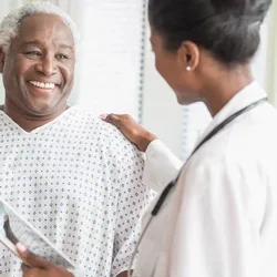 A man in a hospital gown smiles at a doctor in a white lab coat. 