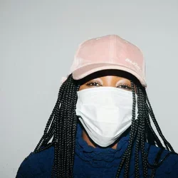 A woman in a pink baseball hat wears a face mask.