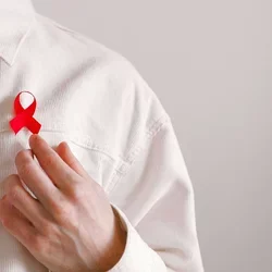 A red AIDS awareness ribbon is pinned on a man's off-white corduroy shirt.