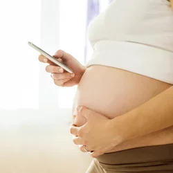 Side view of a pregnant woman holding a phone.