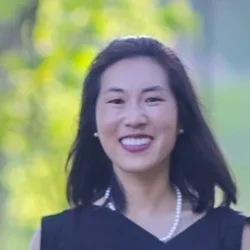 Woman with dark shoulder length hair smiling with green trees in the background