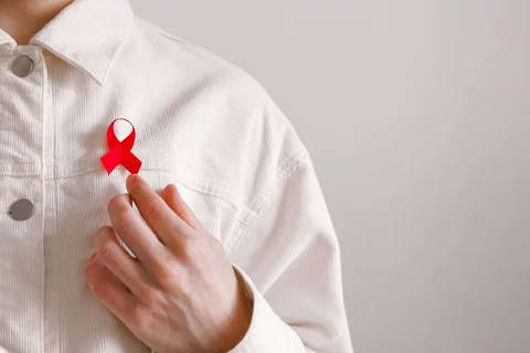A red AIDS awareness ribbon is pinned on a man's off-white corduroy shirt.