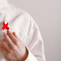 A red AIDS awareness ribbon is pinned on a man's off-white corduroy shirt.